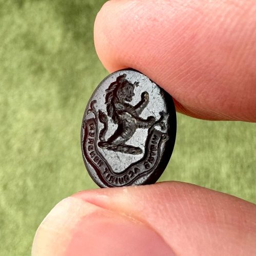 Dark red oval paste glass intaglio with imagery of a detailed heraldic rampant lion above a banner with Latin motto virtus aquirit honorem (virtue acquires honour)