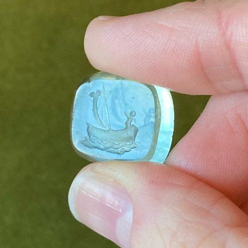 Very pale green paste intaglio with imagery of Cupid in a boat, blowing the sails